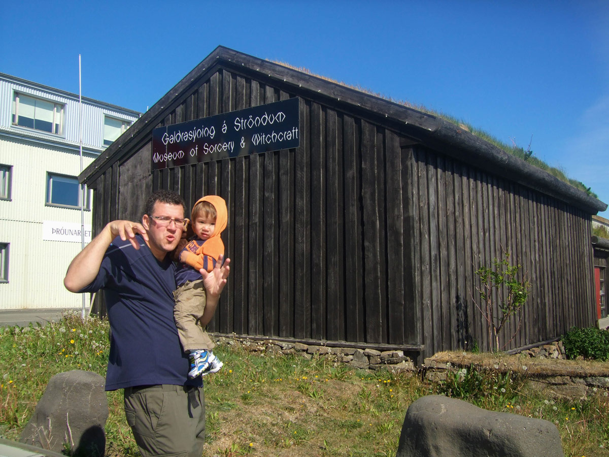 A man makes a funny face while holding a toddler in front of the witchcraft and sorcery museum in Holmavik, Iceland
