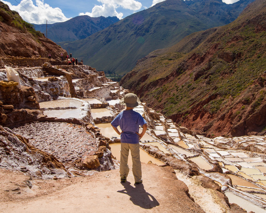 A young boy with his hands on his hips looks out over the salt pans of Maras Peru while Visiting Maras and Moray with kids