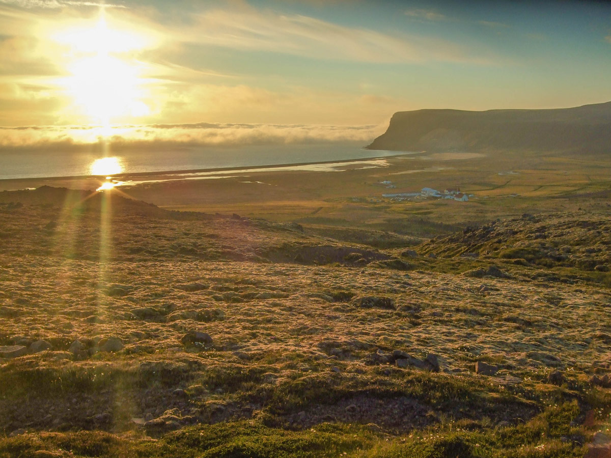 Sunset view of the grasslands and coast of Iceland's westfjords. in the middle is a small hotel with campgrounds