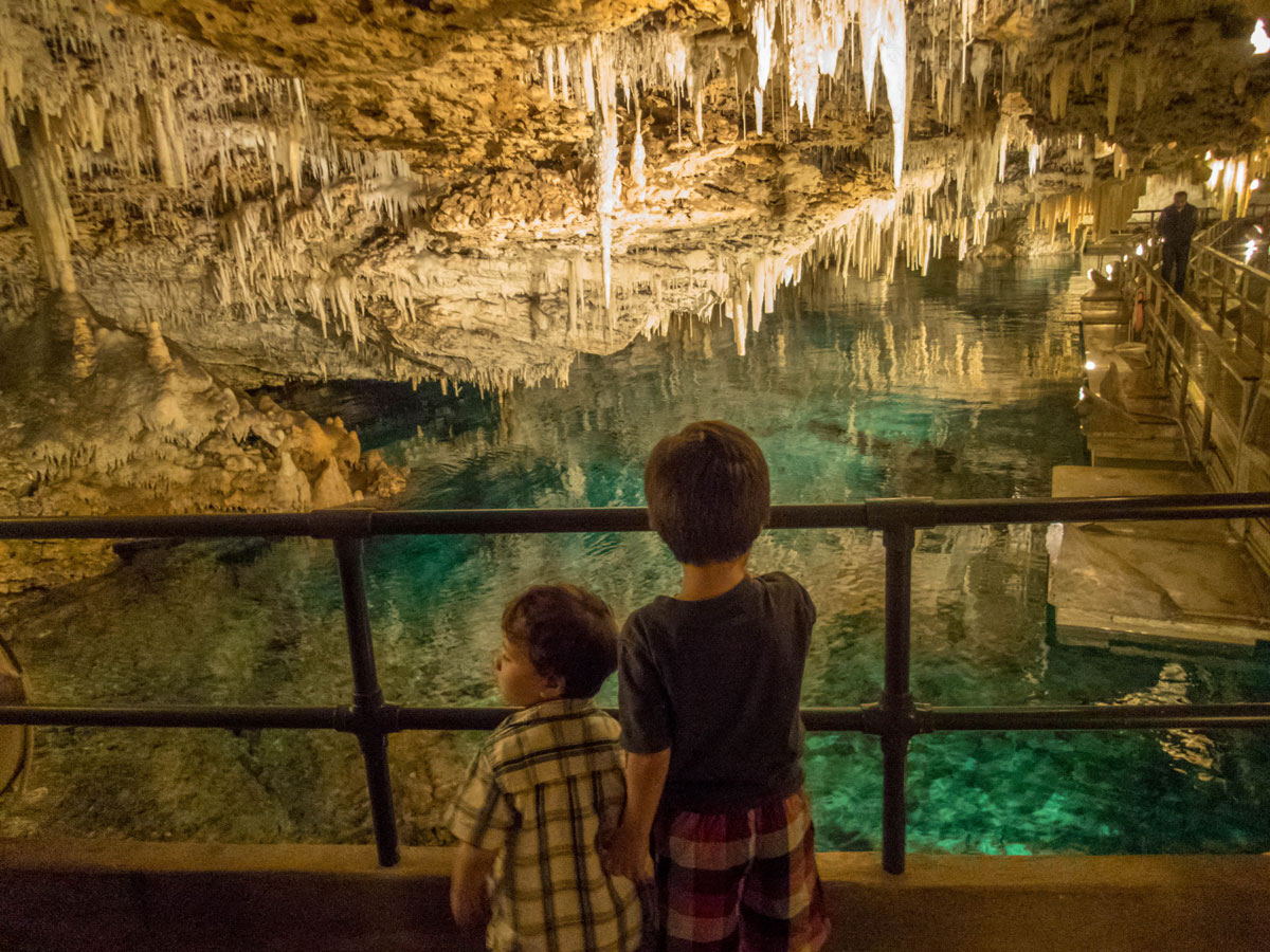 Two boys look out onto a crystal clear pool and stalactites in the Crystal cave in Bermuda with kids