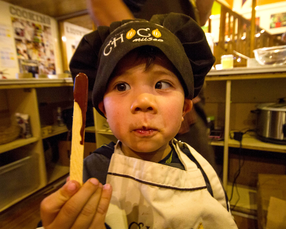 A toddler holds a stick of melted chocolate that he made at the ChocoMuseo in Cusco Peru