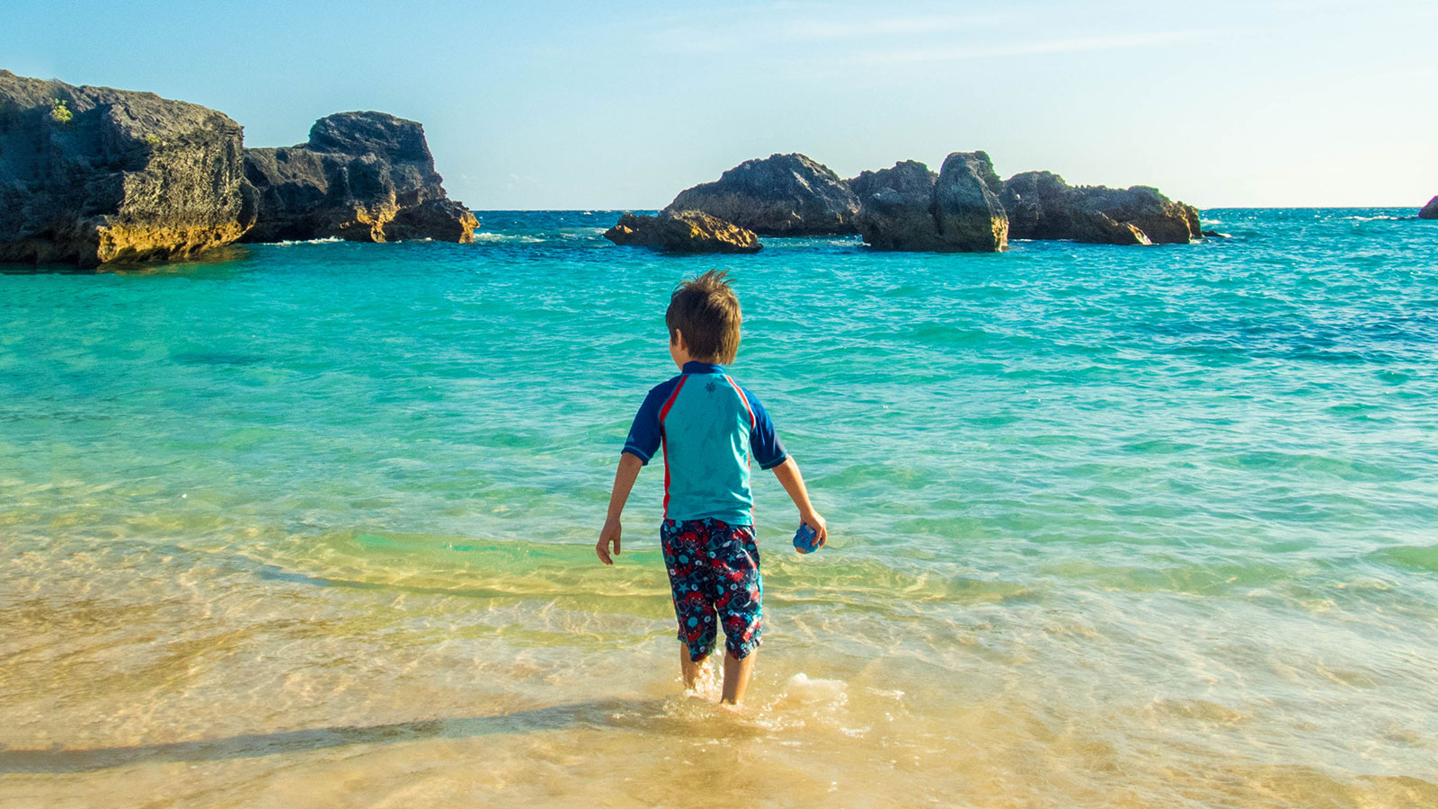 A young boy wades into the waters of Horseshoe Bay Beach, the perfect place to visit in Bermuda with kids