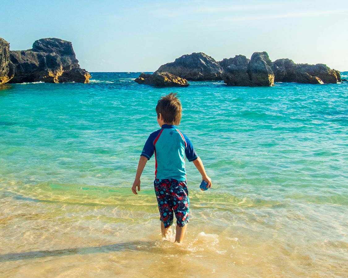 A young boy wades into the waters of Horseshoe Bay Beach, the perfect place to visit in Bermuda with kids