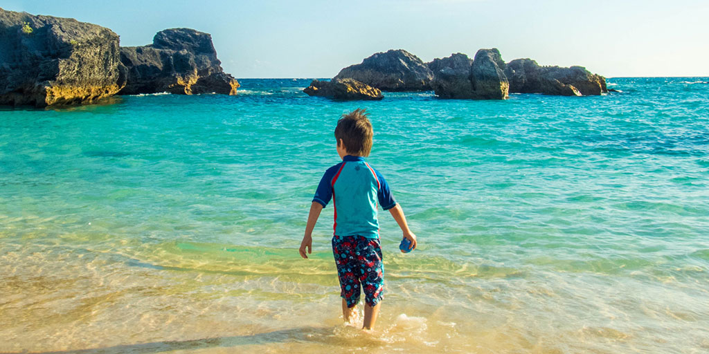 A young boy wades into the waters of Horseshoe Bay Beach, the perfect place to visit in Bermuda with kids