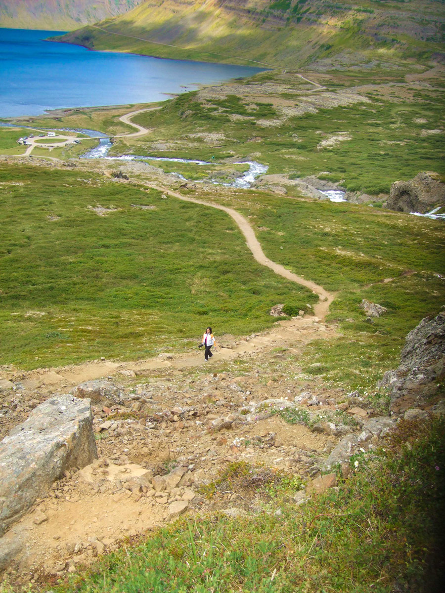 Woman walking along a dirt path among green grass with the ocean in the background