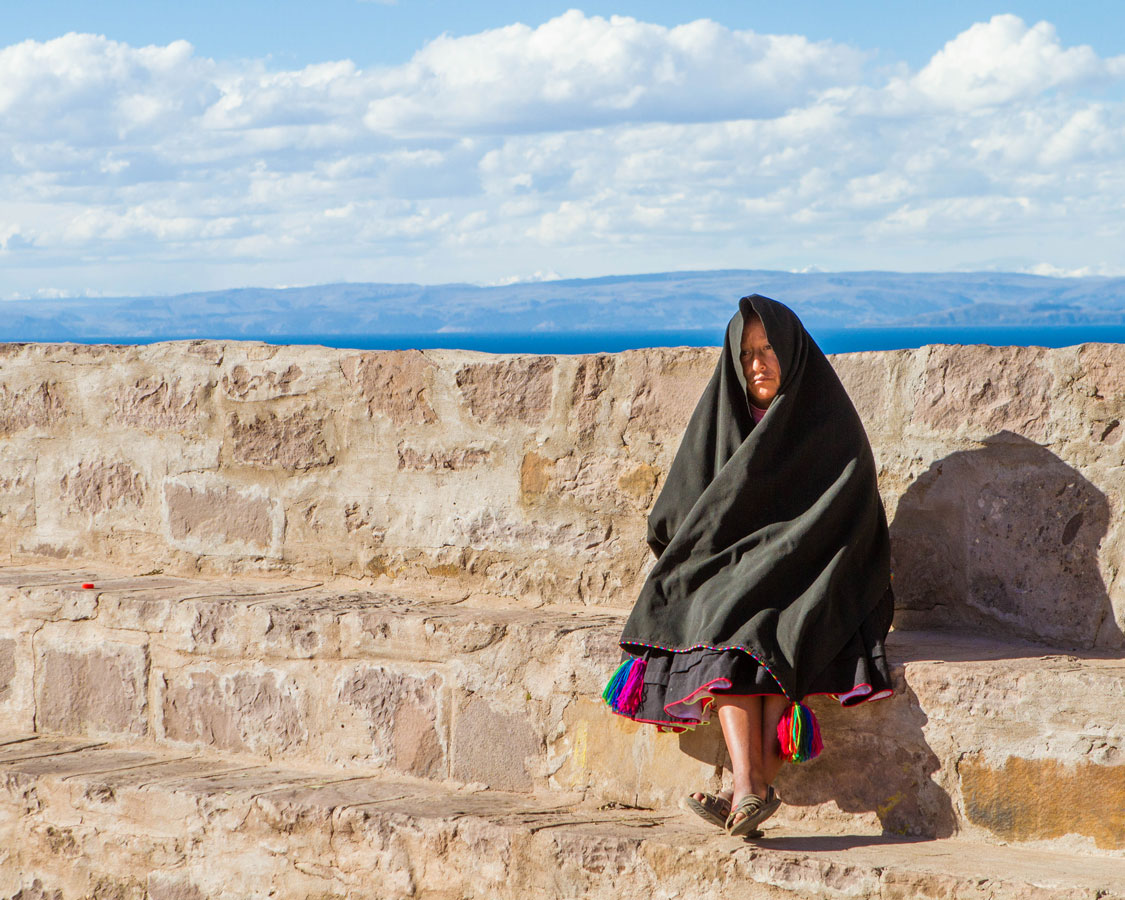 A Taquilenos woman in traditrional clothing sits on a stone wall on Taquile island on Lake Titicaca Peru