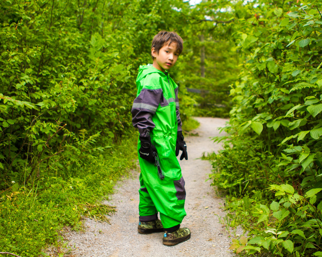 A young boy wearing a green Oakiwear caving outfit looks at the camera during a visit to Bonnechere Caves with kids