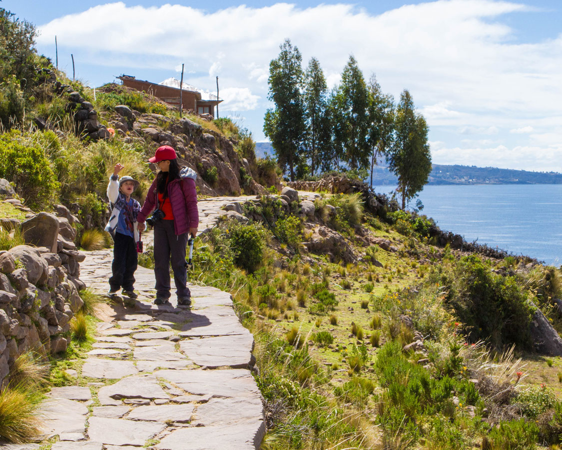While visiting Lake Titicaca with Kids, a woman climbs up the steep walkways of Isla Taquile to visit the local people with her young son