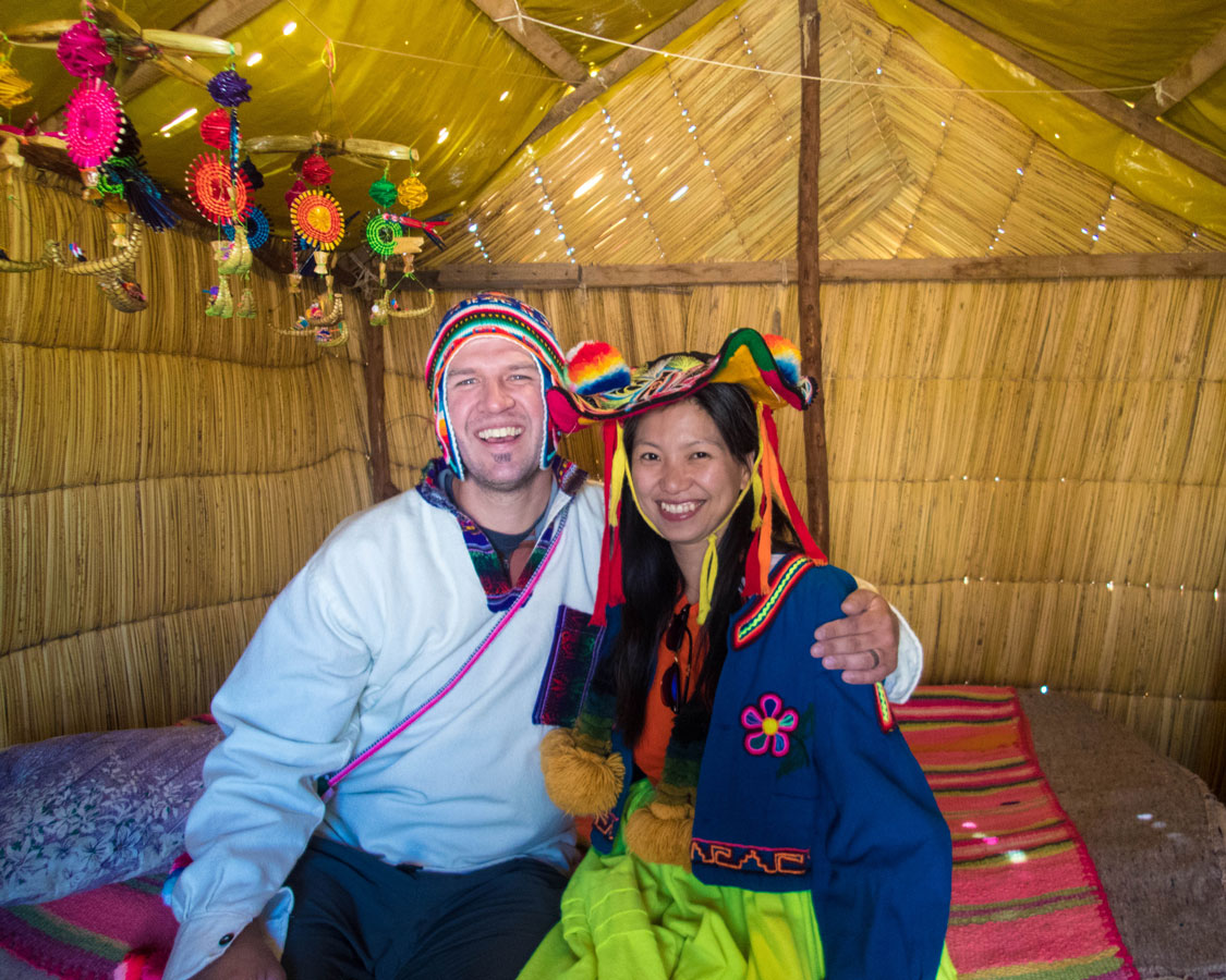 A man and woman smile while wearing traditional Uru clothing while visiting Isla de los Uros on Lake Titicaca with kids