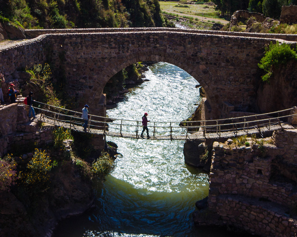 The Cusco to Puno bus stops in Che Cupa where a woman crosses the last Inca rope bridge. A colonial bridge spans the river behind it
