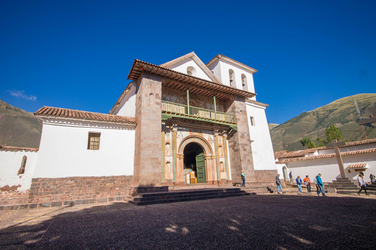 An adobe clad spanish style baroque church with a stone base is lit by the sun in Andahuaylillas Peru