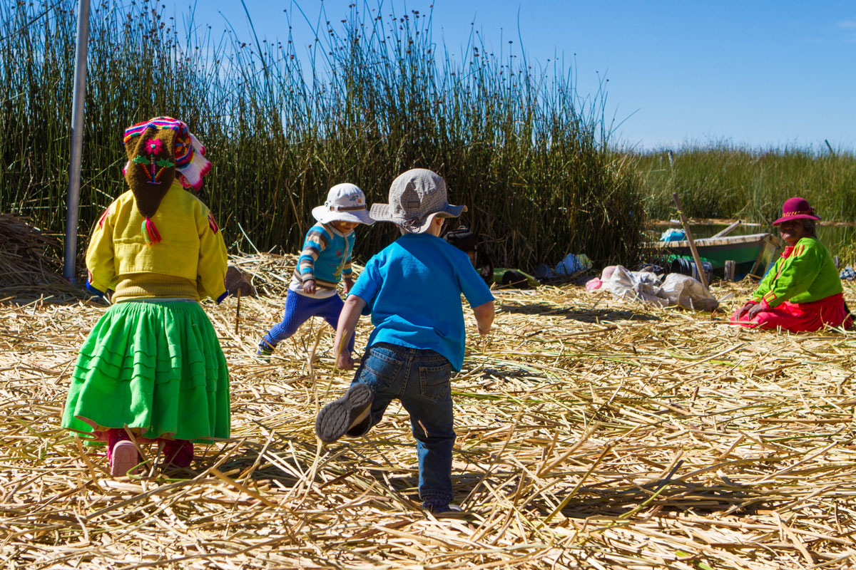 Tourist children play with local Uru children on the reed islands of Lake Titicaca while their family visits Lake Titicaca with kids