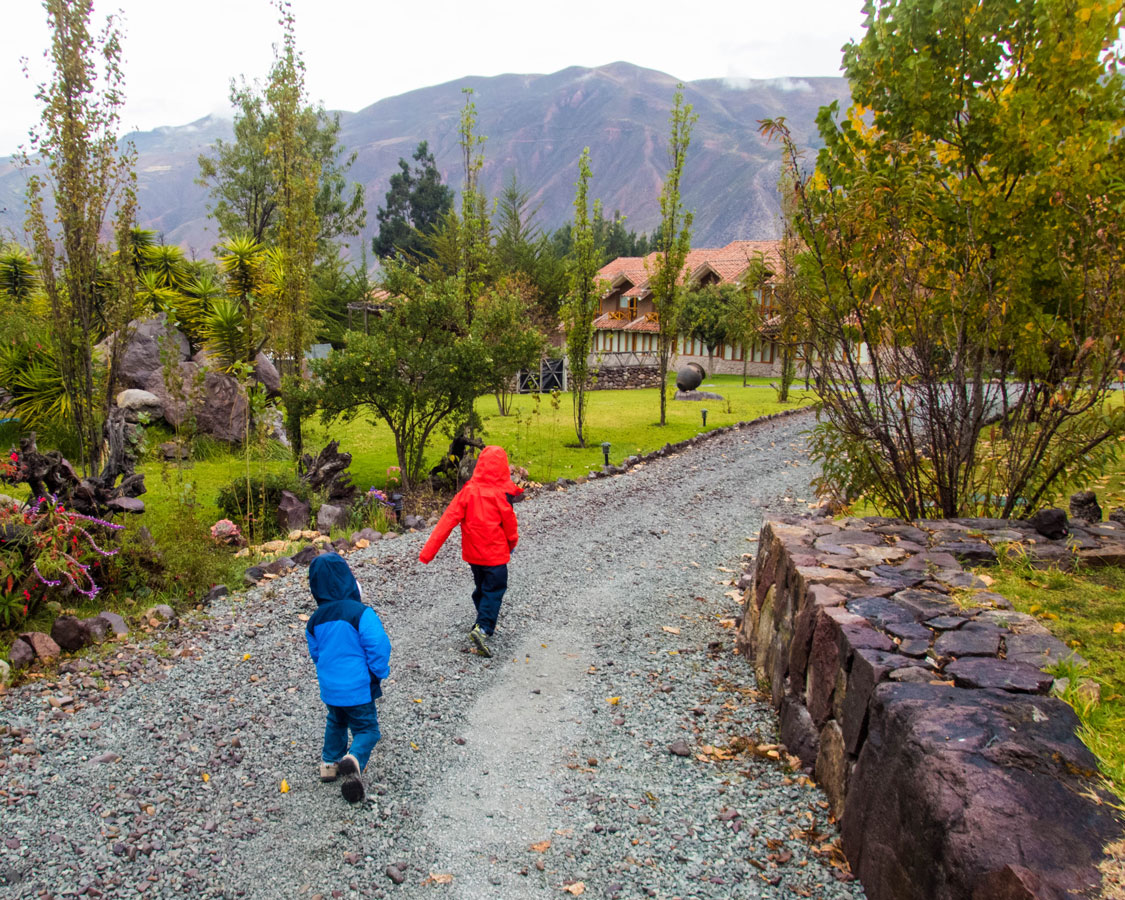 Two young boys wearing colorful rain jackets run along a path at the Casa Andina Private Collection Sacred Valley Peru