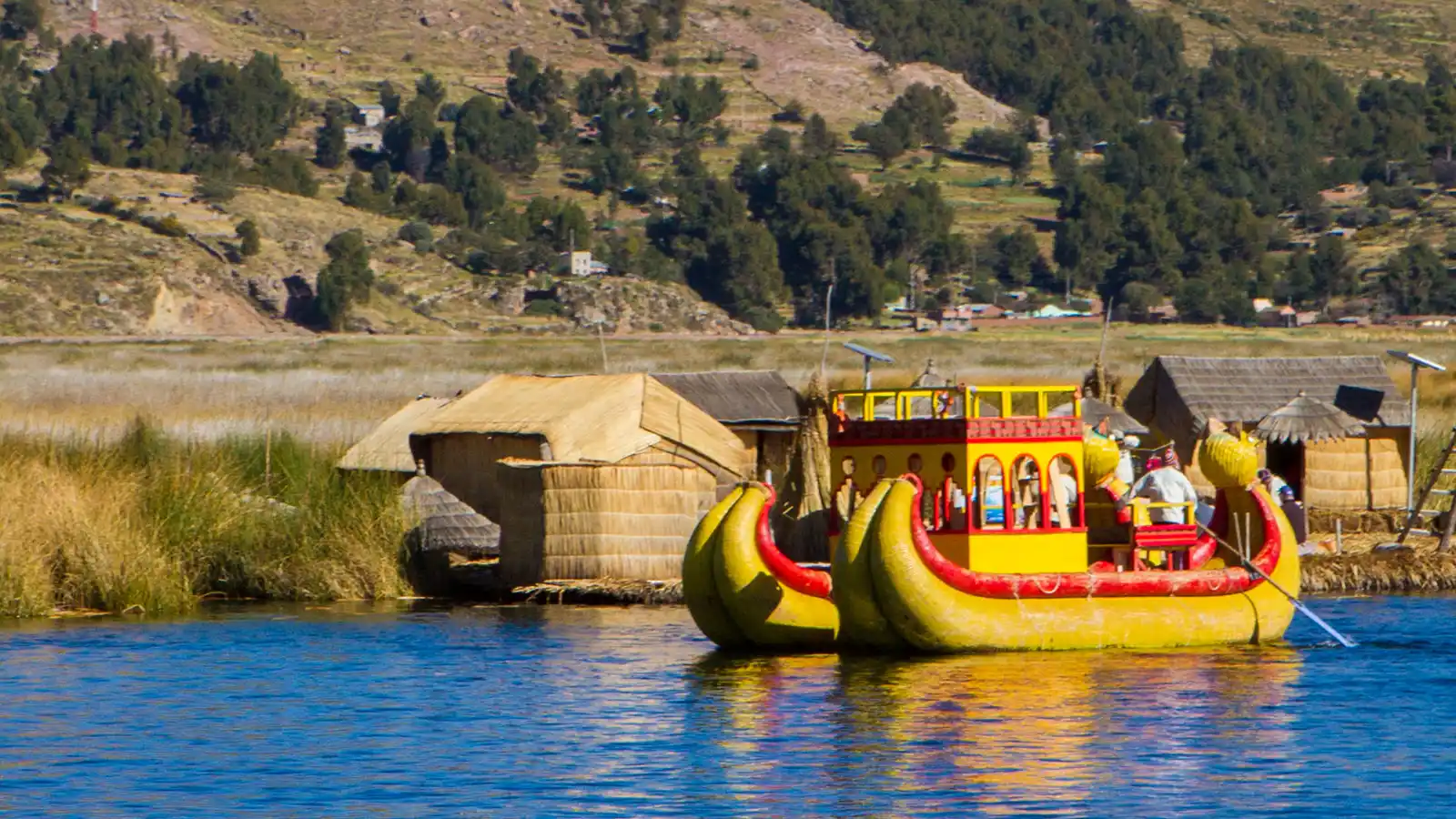 An Uros reed boat floats on the clear blue water of Lake Titicaca, Peru