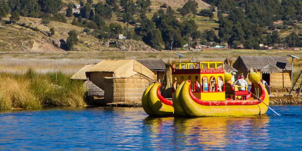 An Uros reed boat floats on the clear blue water of Lake Titicaca, Peru