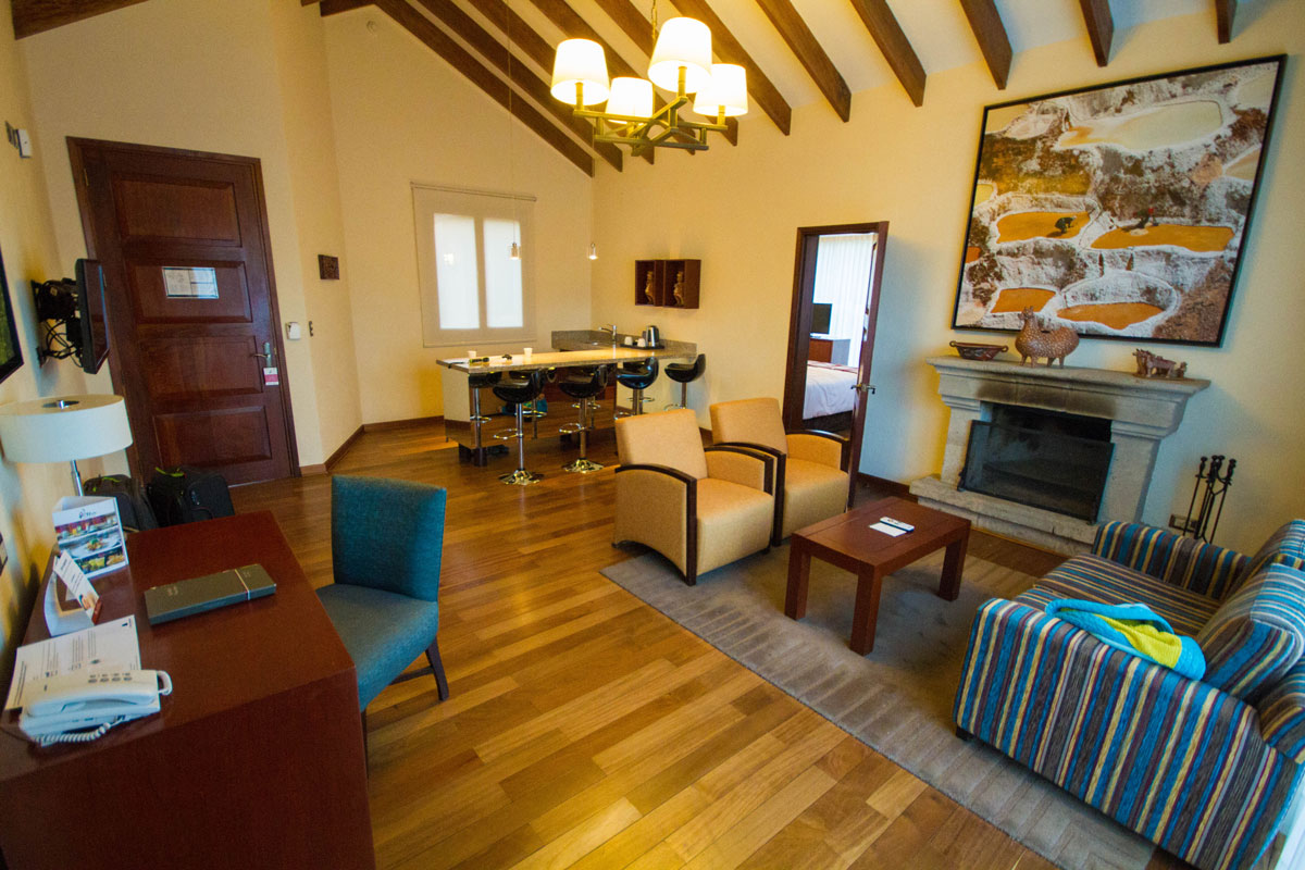 A desk, kitchenette, chairs and and couches sit near a fireplace at the Living room of the Andean Cottage at the Casa Andina Private Collection Sacred Valley Peru