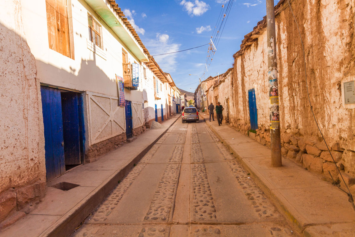A narrow street lined with white adobe buildings with bright blue doors in Maras Peru