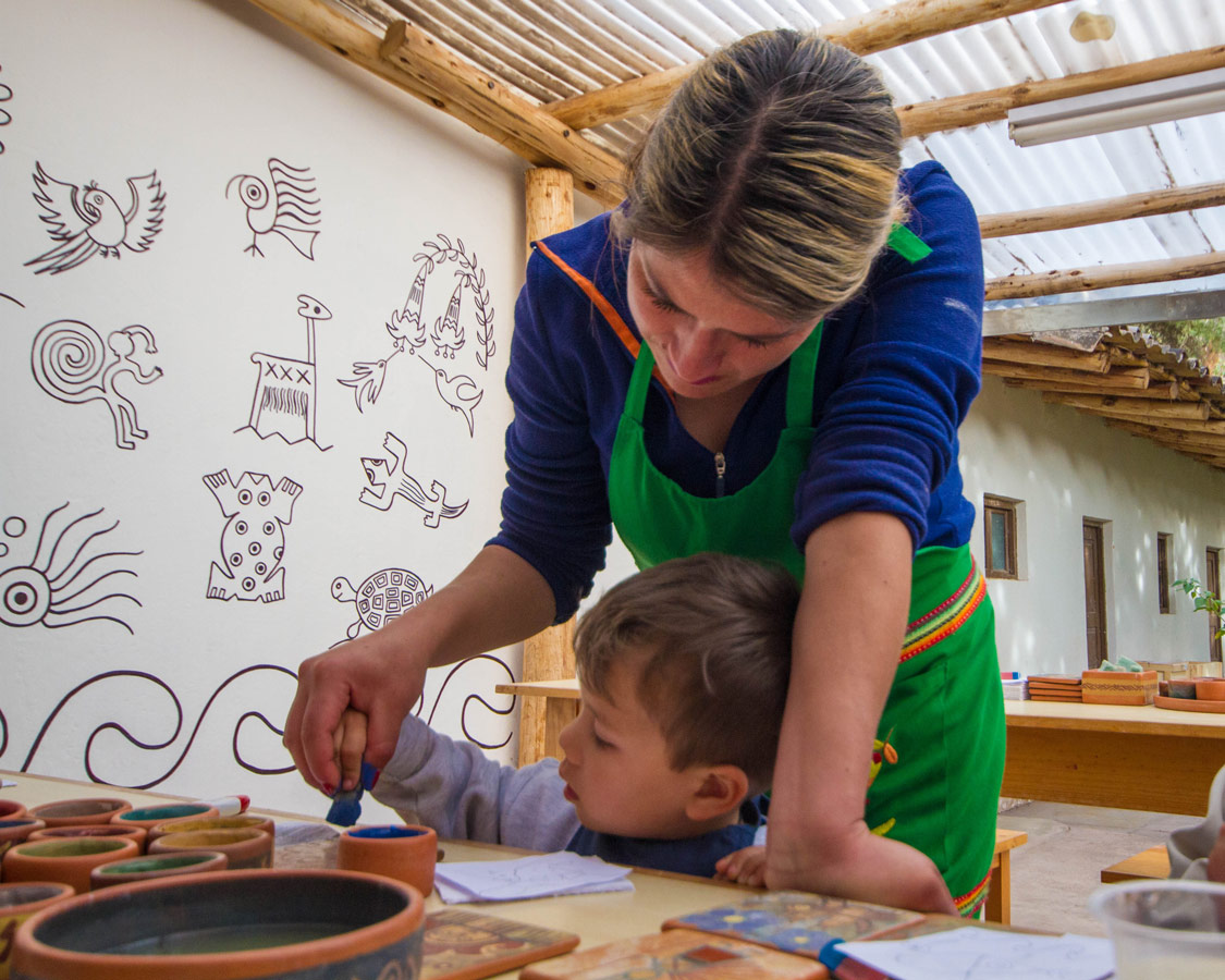 A Ceramic Painting for Kids teacher at Taller Ceramica by Pablo Seminiario helps a toddler work on his pottery painting in Urubamba Peru