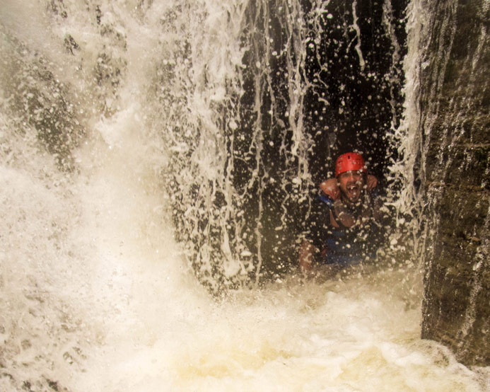 A man in whitewater rafting gear peers out from inside a waterfall at the base of Wolfs Creek in Letchworth State Park in New York State