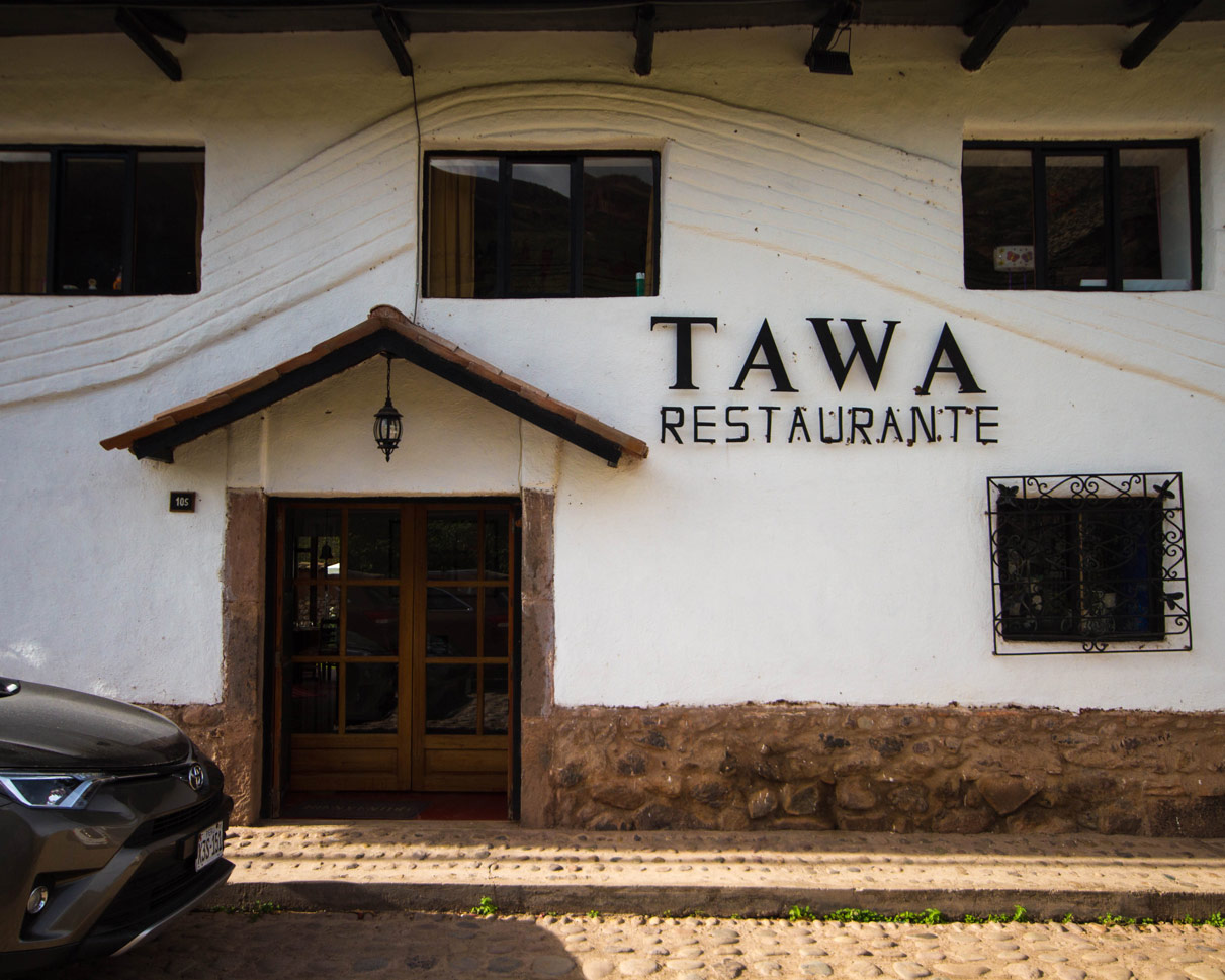 A white adobe building with wood trim in Yucay Peru with a sign reading Tawa Restaurant that we saw on our way to a Ceramics Painting with Kids workshop with Pablo Seminiario