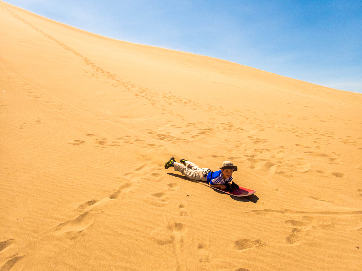 A young boy rides his sandboard down the dunes of Huacachina Peru after exploring Paracas Peru and the Ballestas Islands National Marine Reserve