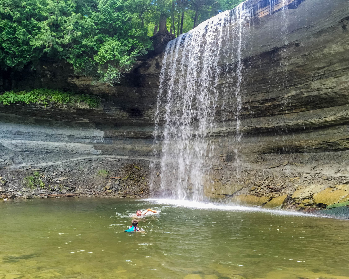 A father and some swim under a waterfall on Manitoulin Island. A swim in Bridal Veil Falls is one of the top things to do on Manitoulin Island