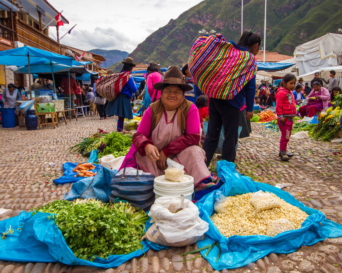 A Quechua woman sells food and grains at the Pisac Market in Peru with kids on a 14 day Peru itinerary