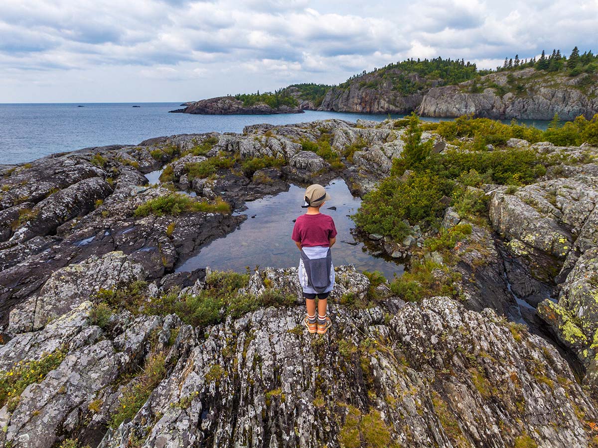 A young boy on a hike stands next to a pool of water at Lake Superior National Park in Ontario