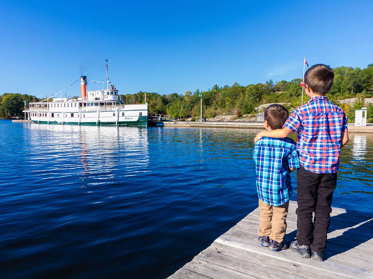 Two boys watch a Lake Muskoka Steamship from a dock in Huntsville Ontario