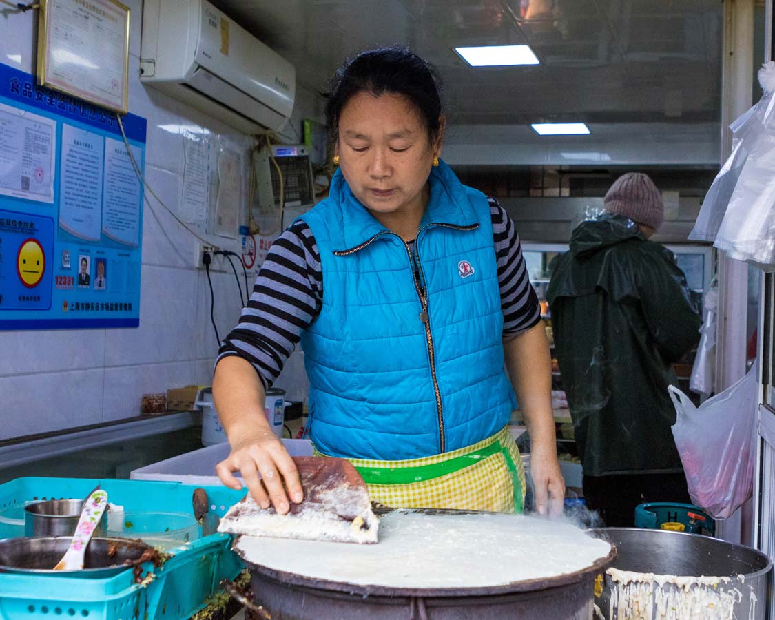 A streetside food vendor prepares wraps at a concession during a Shanghai food tour