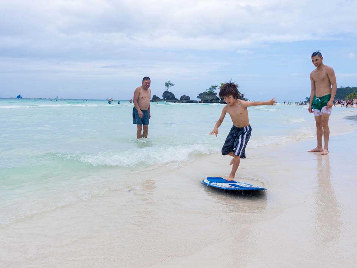 Adults cheer on a young boy skimboarding in Boracay Philippines