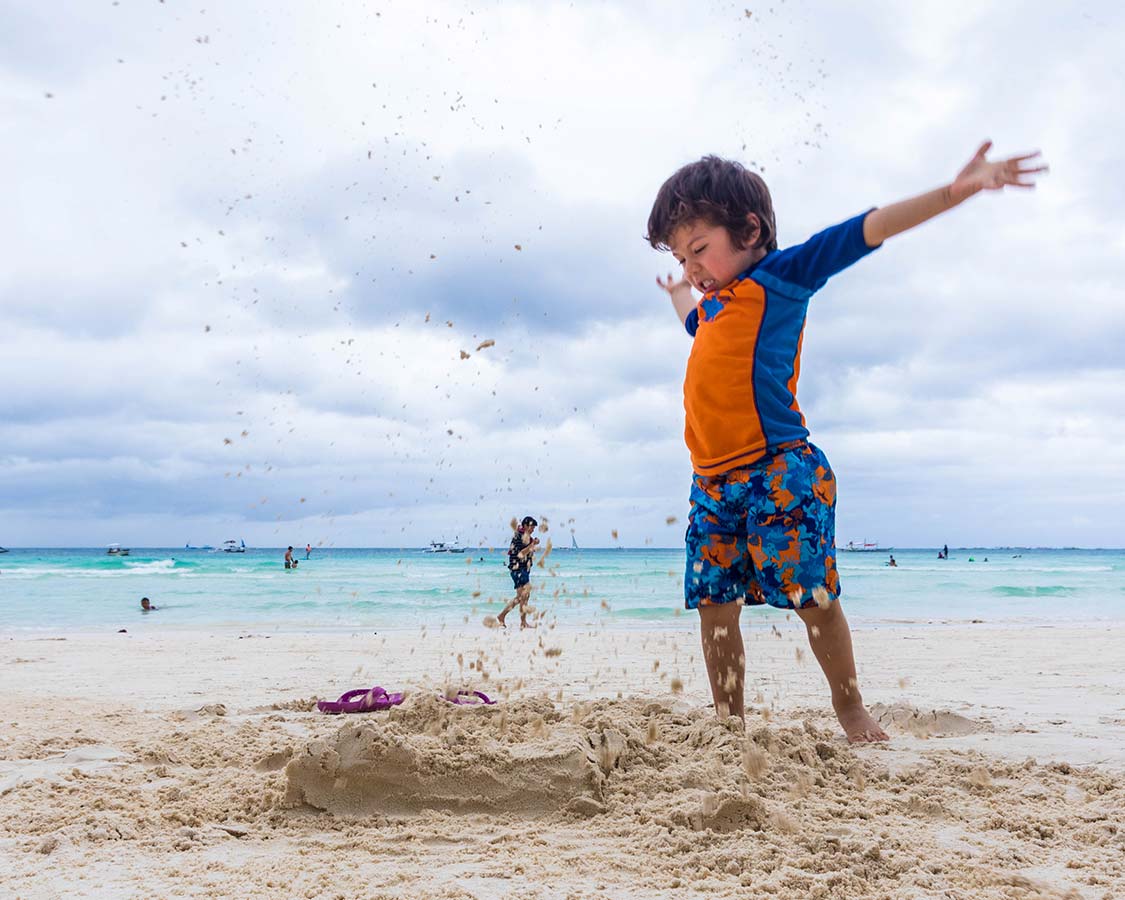 A young boy breaks a sand castle on Whites Beach in Borcay with kids