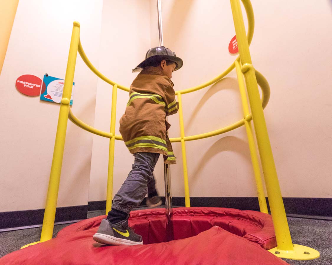 A young boy in a firefighter outfit slides down a pole at the Glazer Children's Museum in Tampa Florida