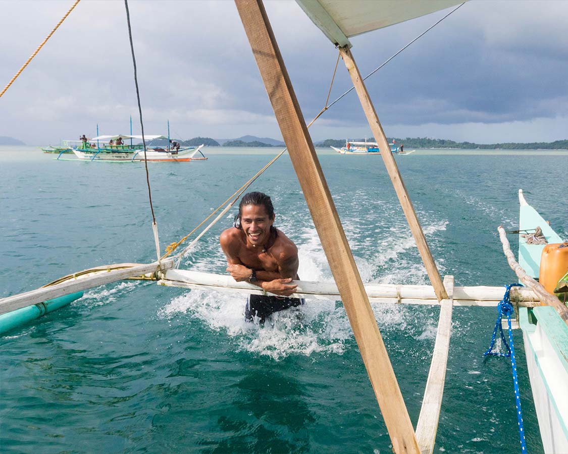 Filipino guide hanging from paraw in San Vicente with Kids