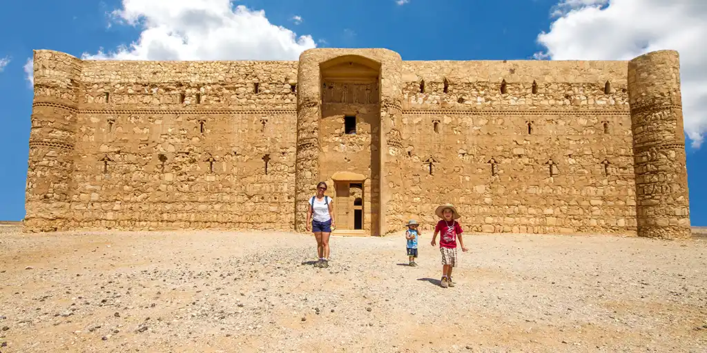 A family walking out of one of the most incredible Desert Castles in Jordan under a clear blue sky