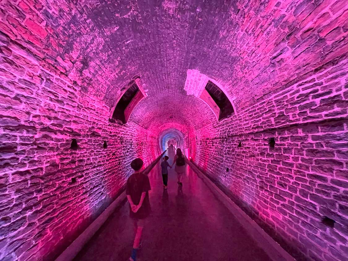 A boy walks through a pink-lit stone railway tunnel in Brockville, Ontario