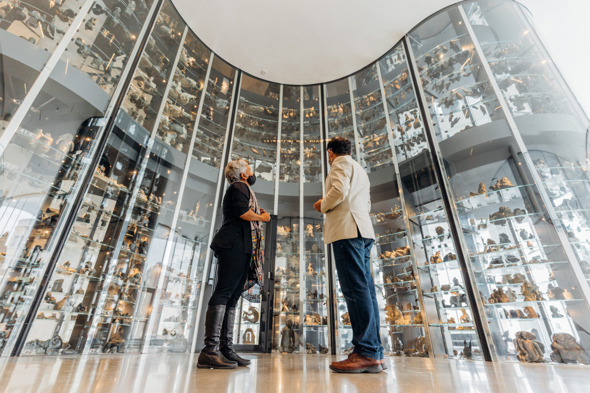 A man and woman look up at a wall of Inuit art at WAG-Qaumajuq