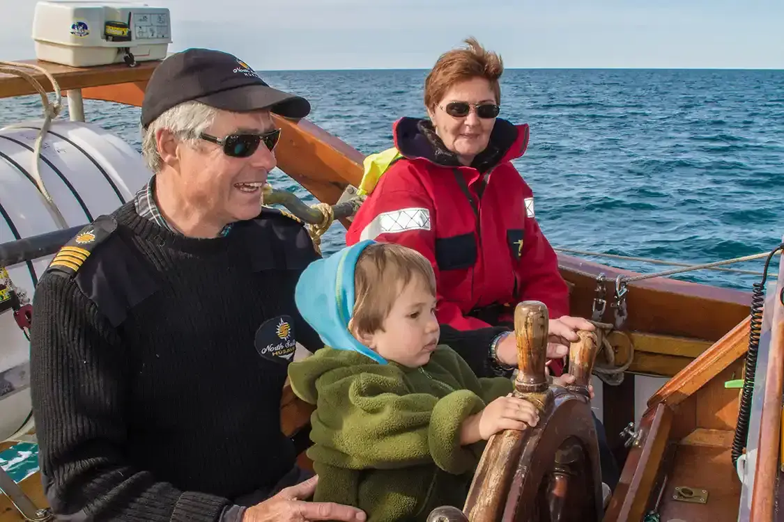 A toddler wearing a fleece mid-layer with the captain of a whale tour in Iceland