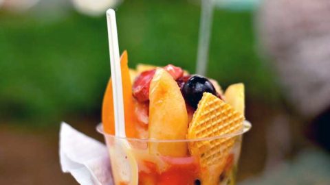Colombian fruit cocktail with mango, cherry, blueberry, and a wafer cracker served in a cup against a blurred green background