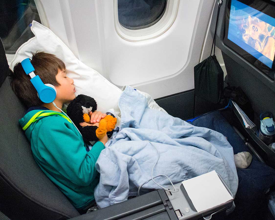 Young boy with a penguin stuffy wearing headphones while sleeping on a plane