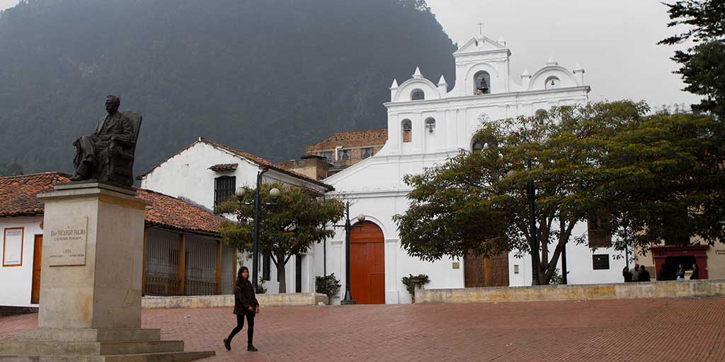 A woman walks past a bell near a white church in Bogota Colombia