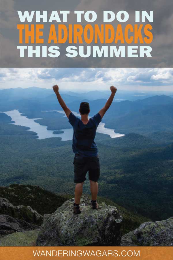 A man standing on top of a mountain looking out over lakes and hill with his arms raised