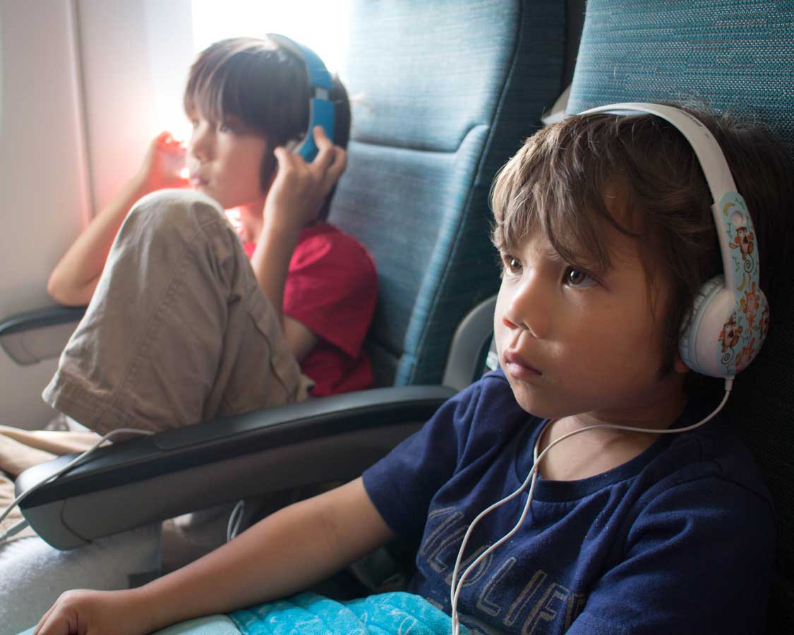 two boys wearing headphones whle watching movies on an airplane