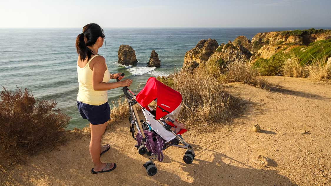Woman pushing the best travel stroller along oceanside cliffs in Portugal