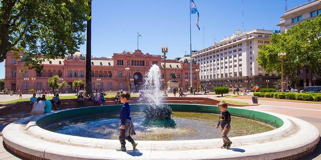 Two young boys walking around a fountain in Paza de Mayo in Buenos Aires with kids