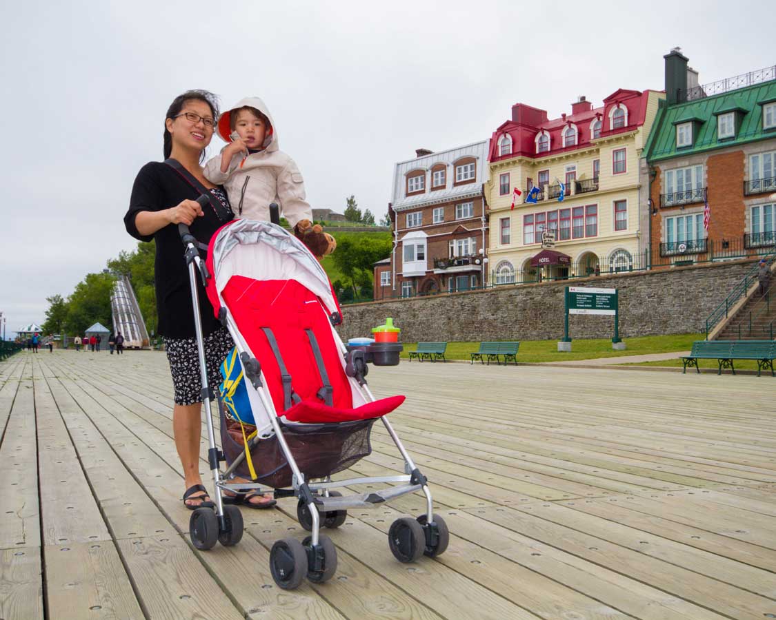 Woman holding a baby while pushing a compact stroller in Quebec City