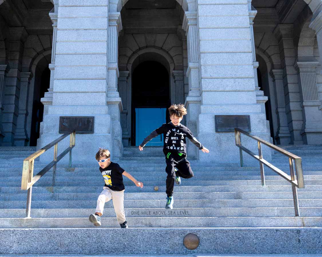 Children jumping from the mile high step at the Colorado Capitol Building in Denver with kids