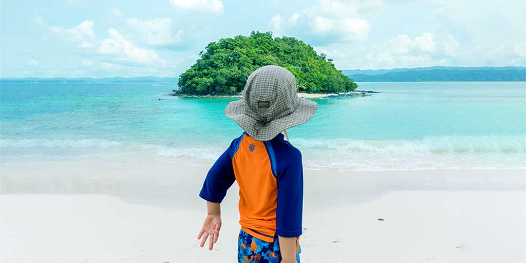 Boy looking at an island from a white sand beach in the Philippines with kids