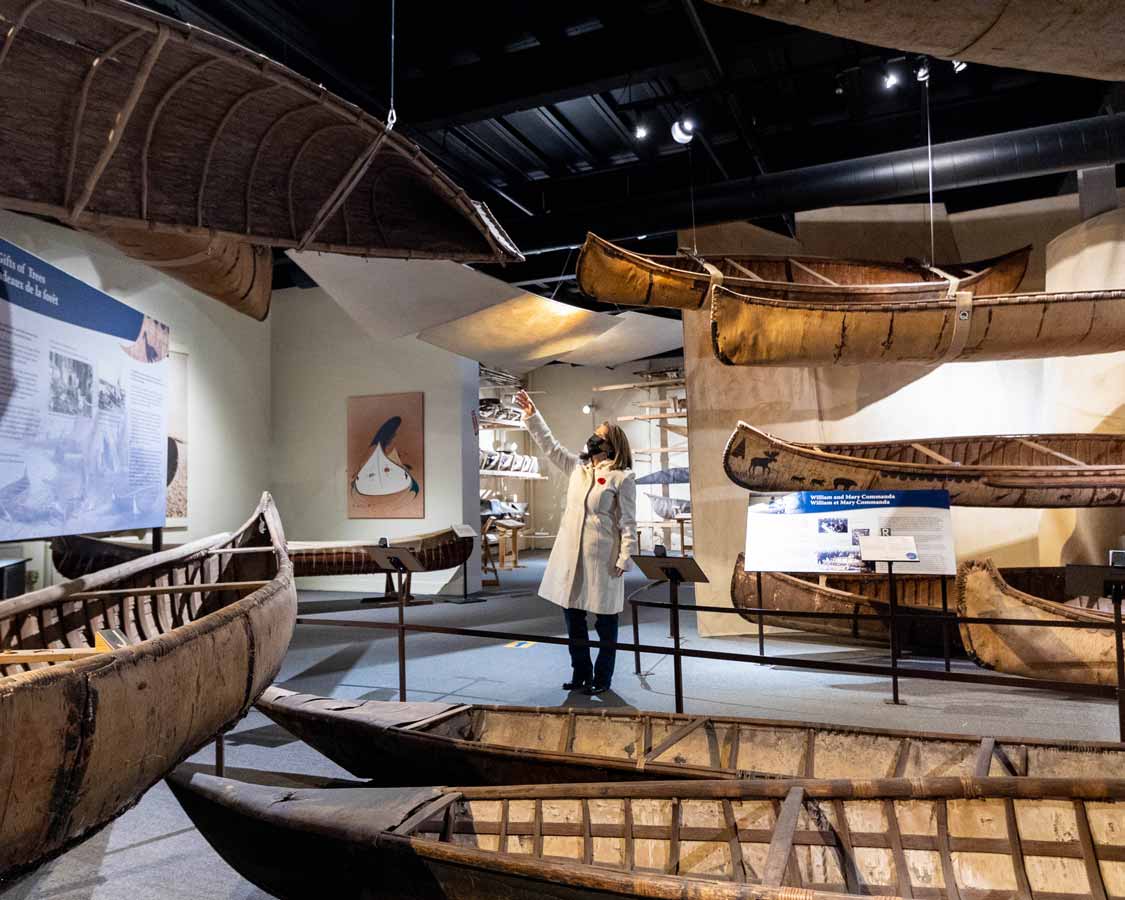 A woman points at a canoe at the Canadian Canoe Museum