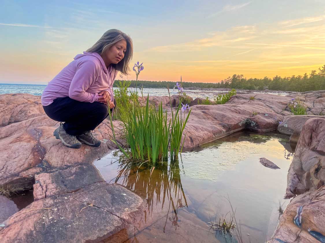 A woman smells flowers by the water in Killarney Ontairo